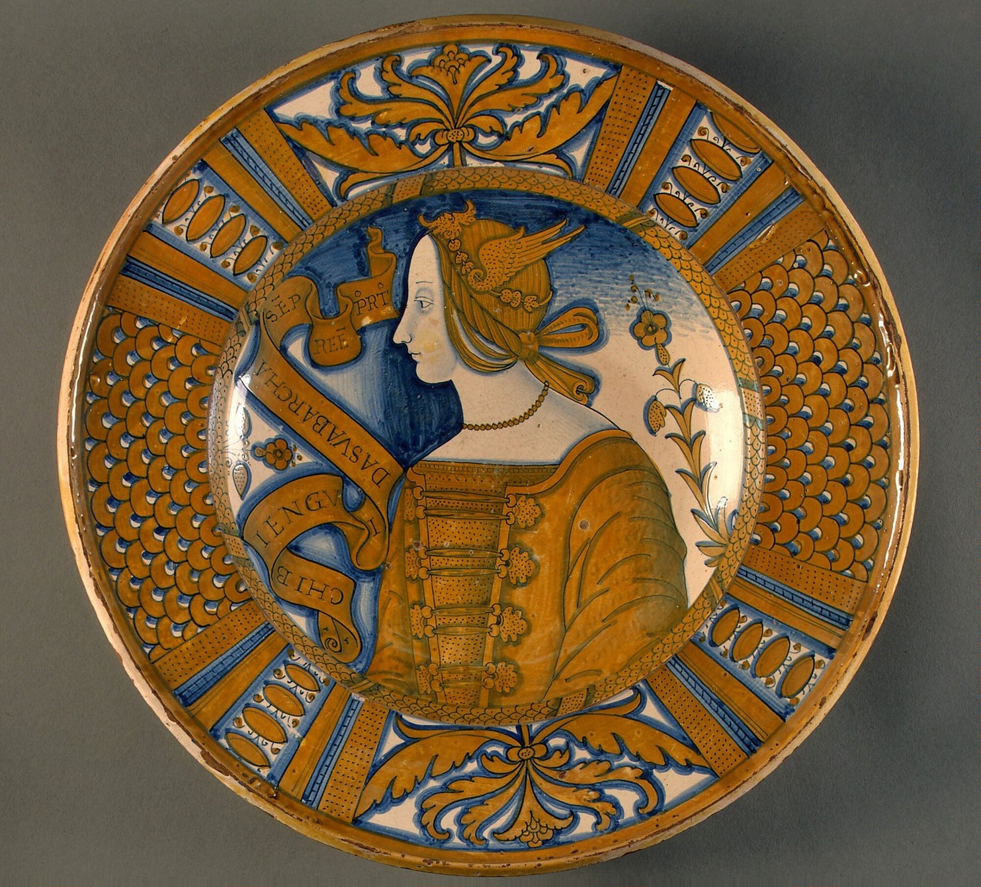 Large dish with segmental border of plant sprays and scale pattern; in the center, a profile bust of a woman in a winged headdress